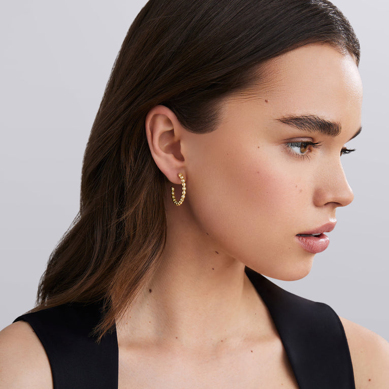 Close-up of a woman wearing gold hoop earrings against a neutral background