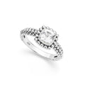 A silver ring featuring a cushion-cut white topaz gemstone surrounded by a beaded halo, with a textured beaded band, shown on a white background.