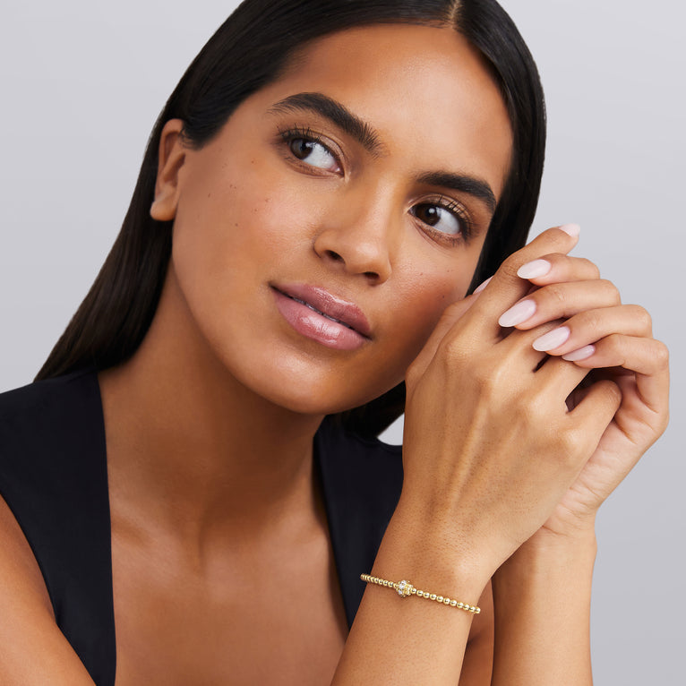 Woman wearing a gold bracelet on a gray background