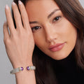Woman's face with a focus on the Rittenhouse Amethyst Cuff Bracelet 12mm, showing textured metal and purple gemstone accents against her wrist.