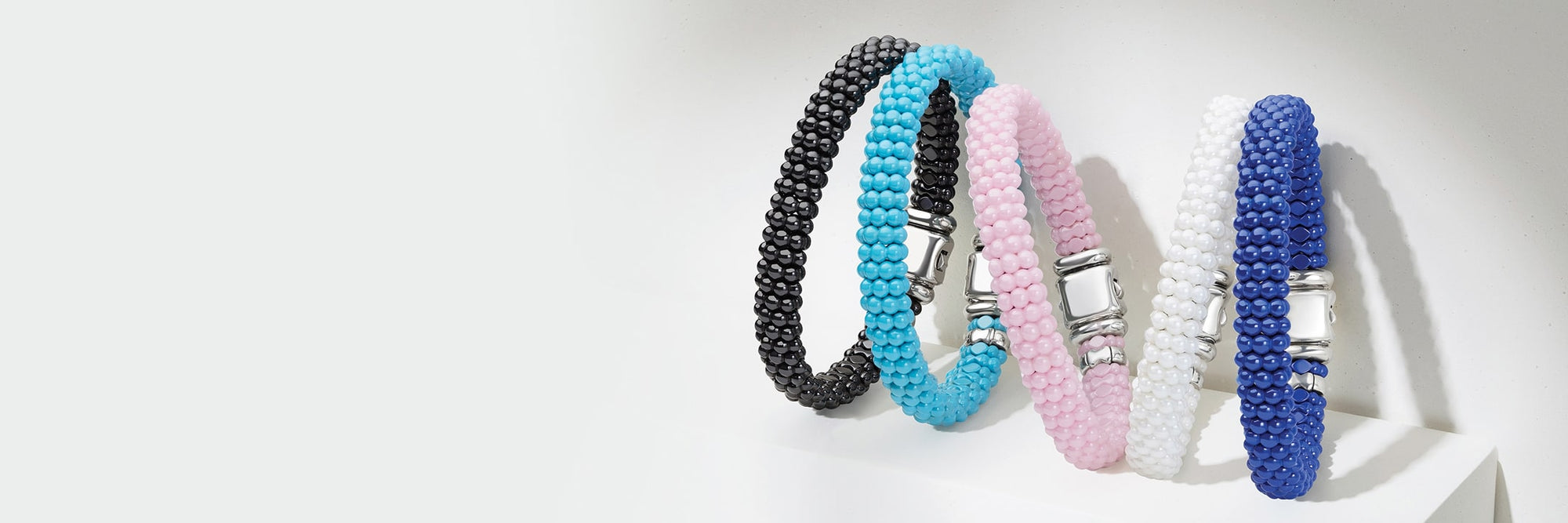 Three beaded bracelets in pink, blue, and black on a light gray background