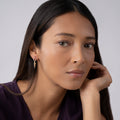 Person wearing KSL Drop Pyramid Hoop Earrings featuring 18K gold and sterling silver Caviar beading, with a dangling pyramid charm against a light gray background.