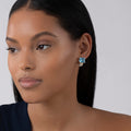 Close-up of a woman wearing Glacier Large Swiss Blue Topaz Huggie Earrings with vibrant blue gemstones in sterling silver and 18K gold Caviar beading by LAGOS.