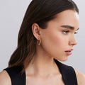 Close-up of a woman wearing gold hoop earrings against a neutral background