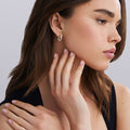 Woman wearing 18K Gold huggie earrings with bezel-set diamonds on white background 