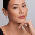 Woman modeling Rittenhouse Amethyst Drop Earrings, featuring a purple gemstone bezel-set in 18K gold and sterling silver with Caviar accents, highlighting LAGOS's elegance.