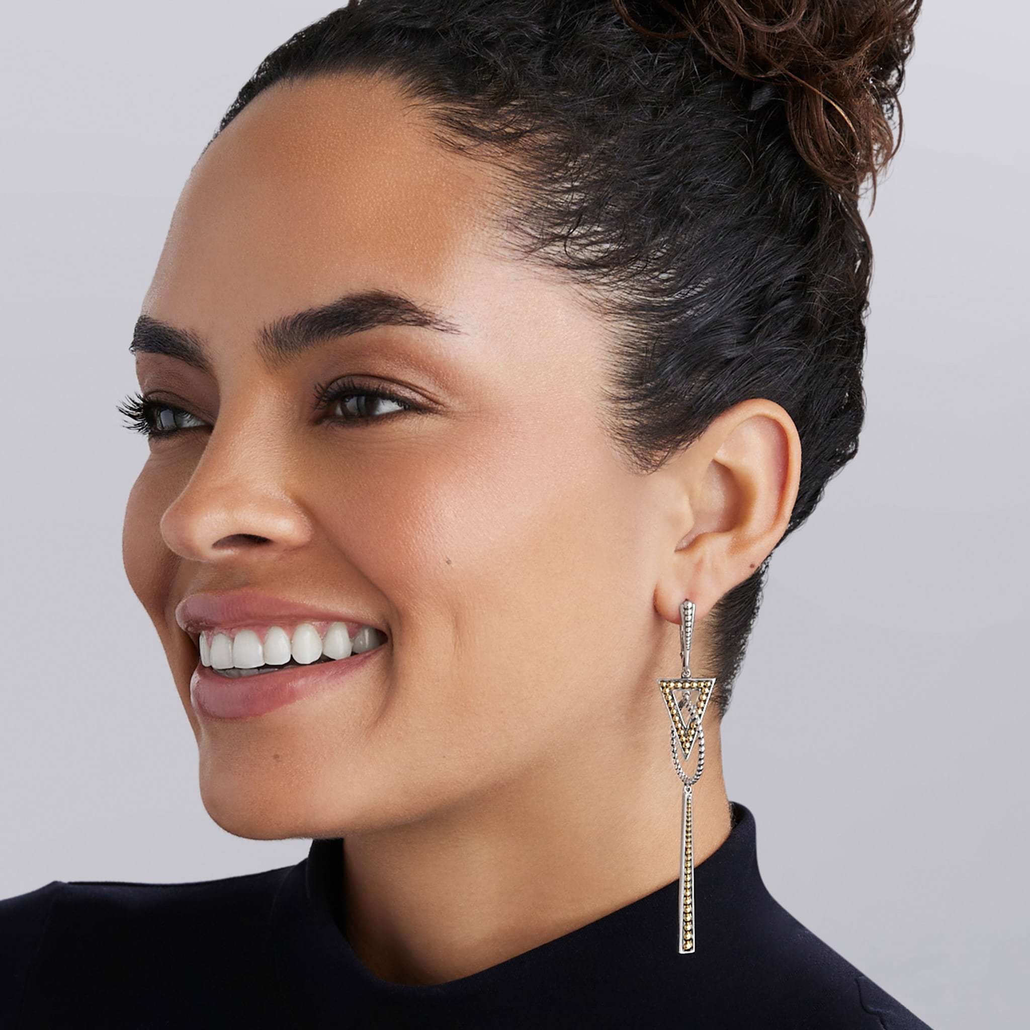 Smiling person showcases Signature Caviar Two-Tone Triangle Circle Drop Earrings, featuring intricate gold and silver triangular motifs with fine chain details.