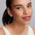 Woman wearing Signature Caviar Two-Tone X Caviar Stud Earrings; gold-and-silver textured studs in X design, showcasing elegance and modern dimension. Hair pulled back, light top visible.