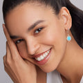 Close-up of a smiling person wearing Maya Small Ceramic Circle Drop Earrings with turquoise stone and sterling silver Caviar beading, highlighting elegance and craftsmanship.