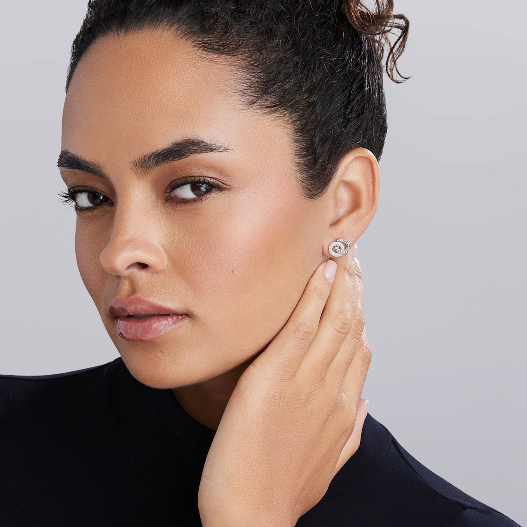 Young woman wearing Signature Caviar Silver Interlocking Diamond Stud Earring, showcasing the elegant design with shimmering diamonds set in sterling silver.