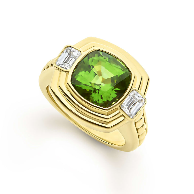 Featuring a cushion-cut peridot gemstone, framed by two baguette diamonds, the 18k gold setting highlights the vibrant green hues of peridot, creating a sophisticated and eye-catching piece.