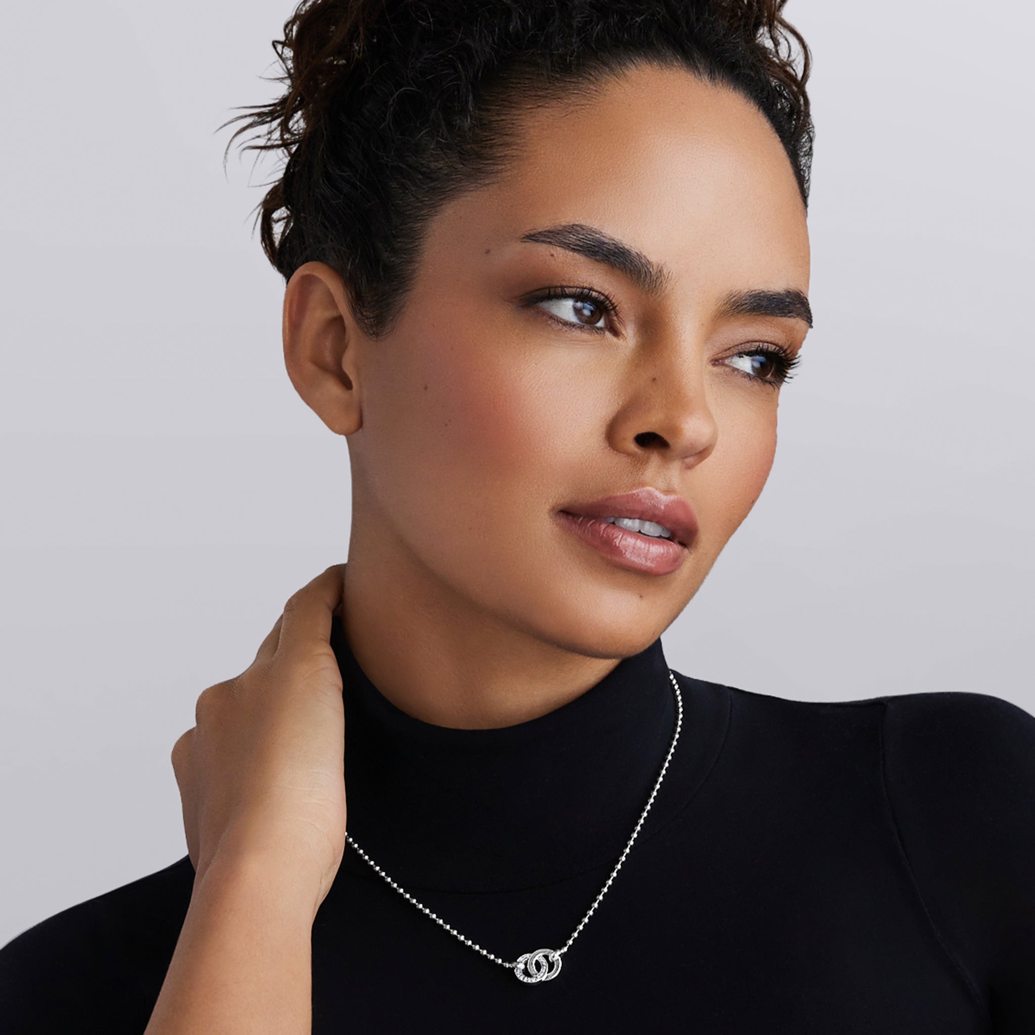 Woman wearing the Signature Caviar Silver Interlocking Diamond Pendant Necklace, showcasing its elegant intertwined design and shimmering diamonds, capturing LAGOS timeless elegance.