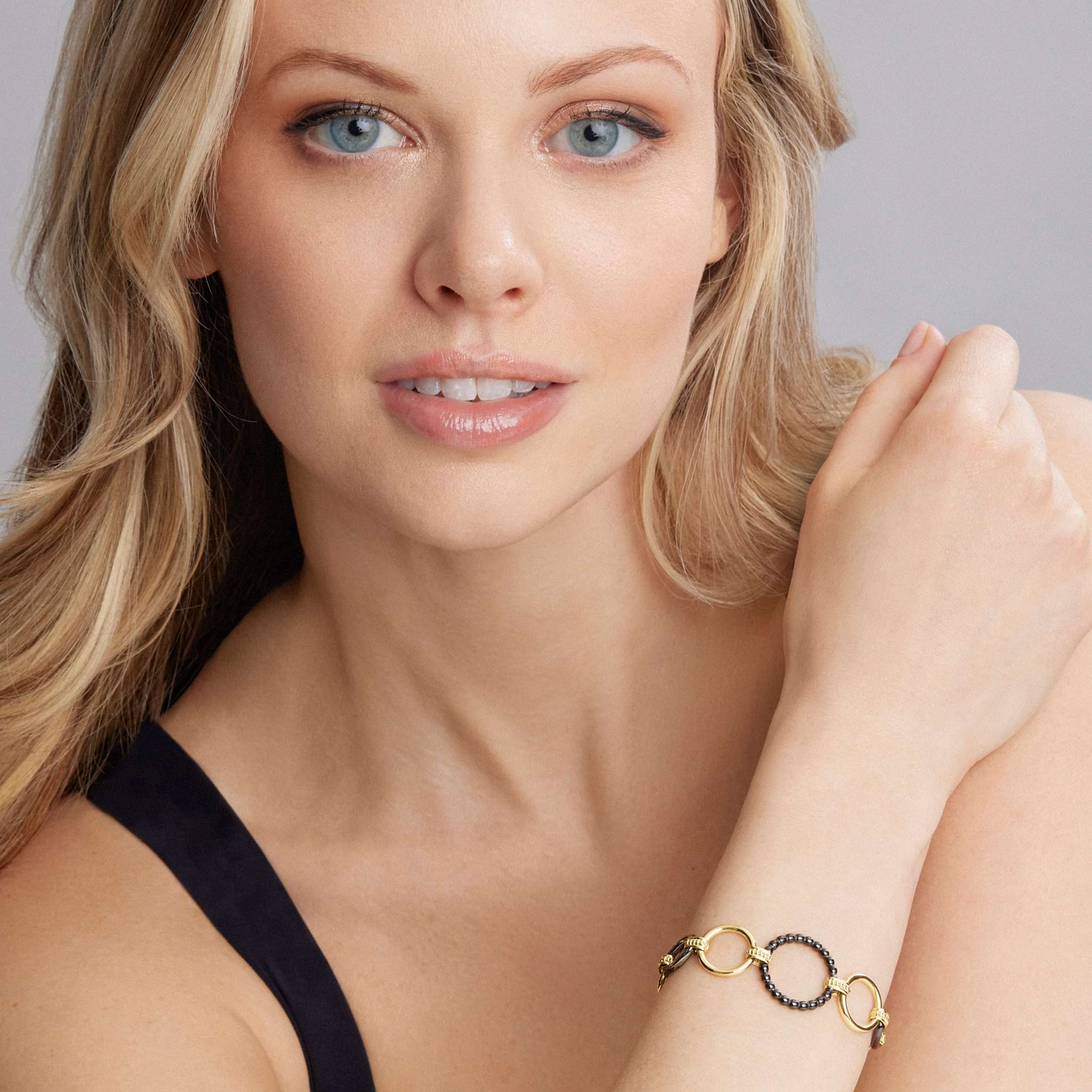 Young woman wearing Meridian 18K Gold and Black Ceramic Link Bracelet, featuring interlocking gold rings and dark beads, on her forearm against a light gray background.
