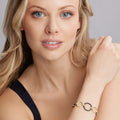 Young woman wearing Meridian 18K Gold and Black Ceramic Link Bracelet, featuring interlocking gold rings and dark beads, on her forearm against a light gray background.