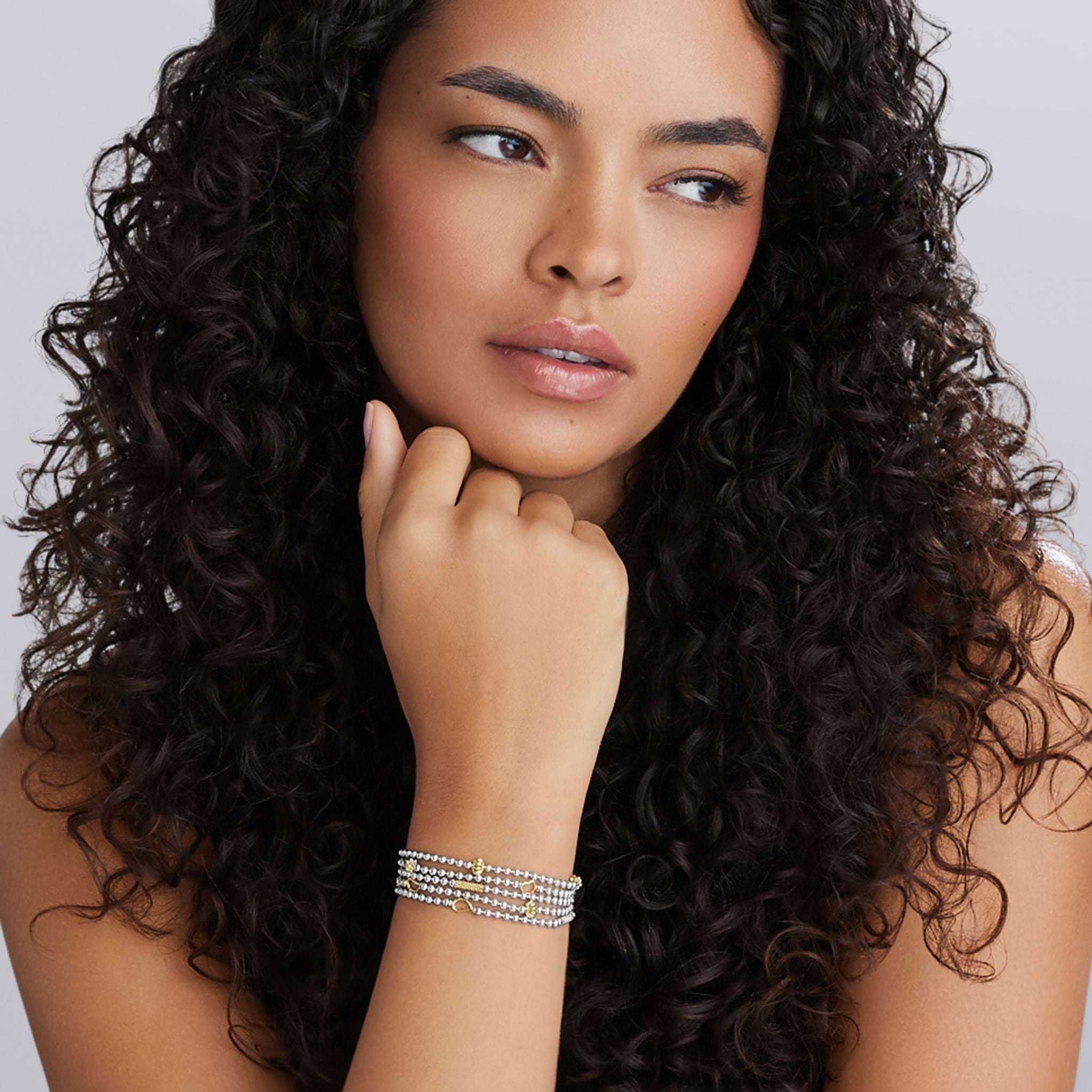 Young woman wearing the Caviar Icon Two-Tone Caviar Five Strand Chain Bracelet, showcasing its layered silver strands with gold accents and Caviar beading, reflecting LAGOS elegance.