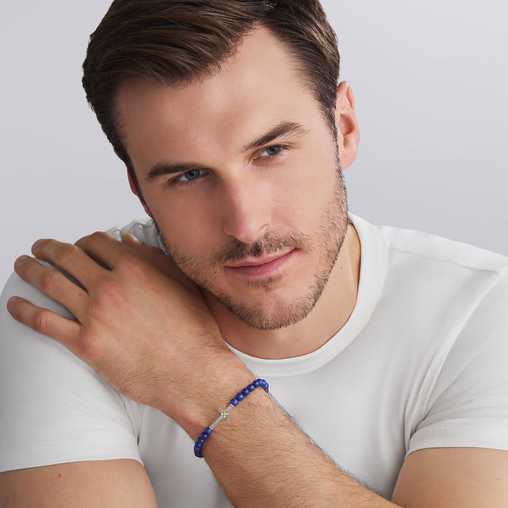 Man wearing a white t-shirt and blue beaded bracelet on a light gray background