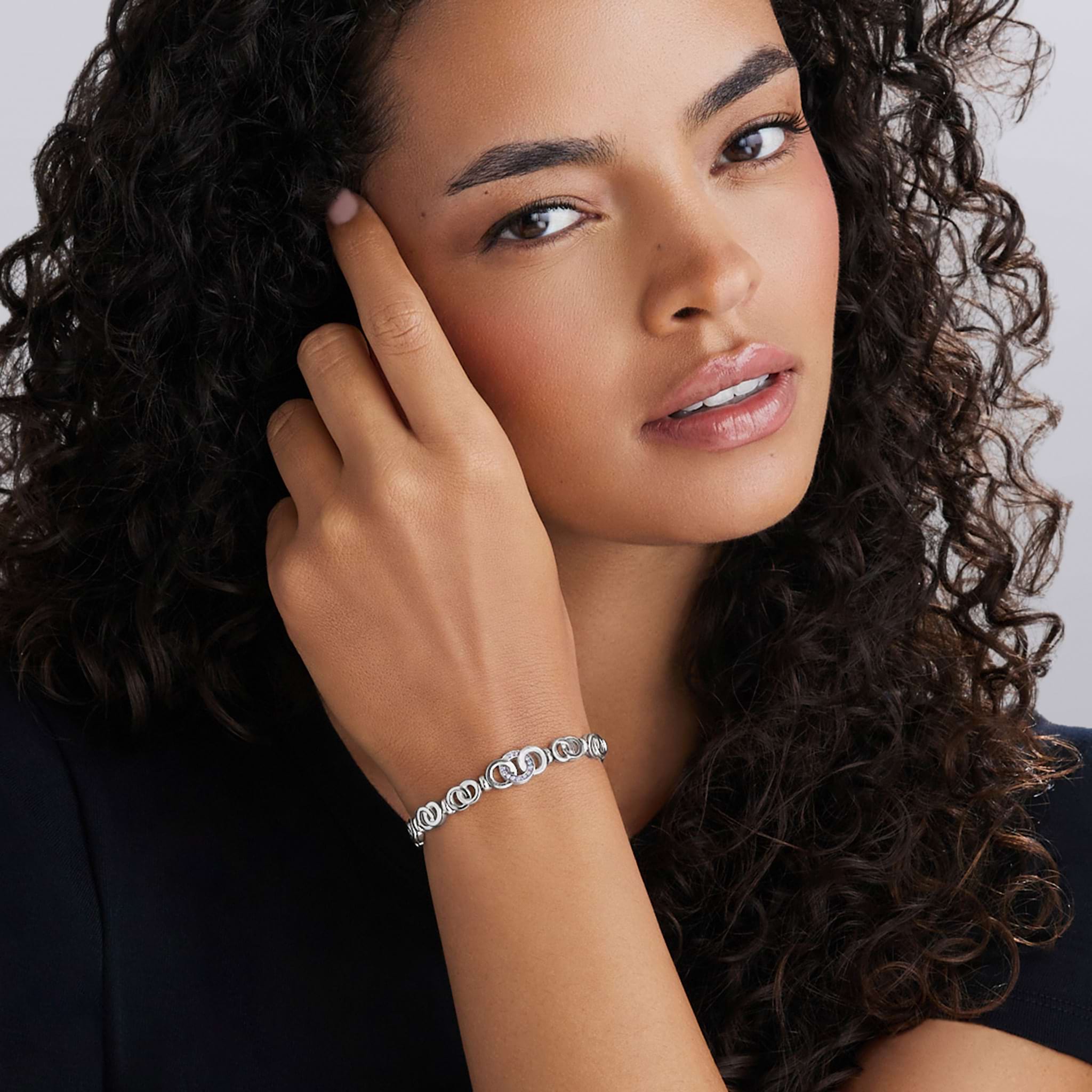 A young woman showcases the Signature Caviar Silver Petite Interlocking Diamond Link Bracelet, highlighting its elegant interlocking links and sparkling diamonds on her wrist.