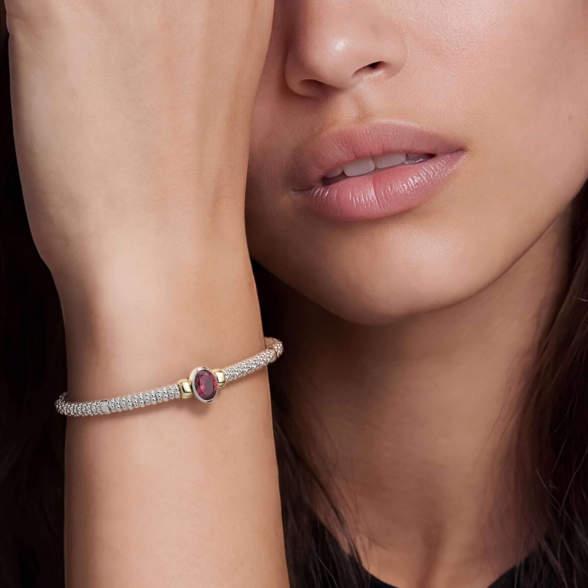 Woman wearing the Signature Caviar Two-Tone Garnet Oval Mini Versa Torque Bracelet, featuring 3mm sterling silver caviar beading, garnet gemstone, and 14K gold accents.