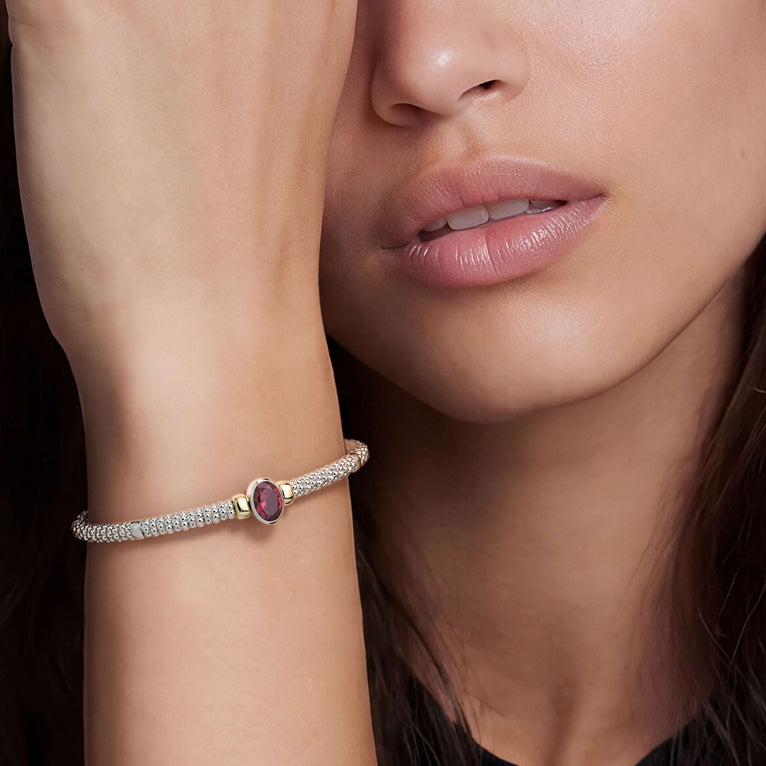 Woman wearing the Signature Caviar Two-Tone Garnet Oval Mini Versa Torque Bracelet, featuring 3mm sterling silver caviar beading, garnet gemstone, and 14K gold accents.