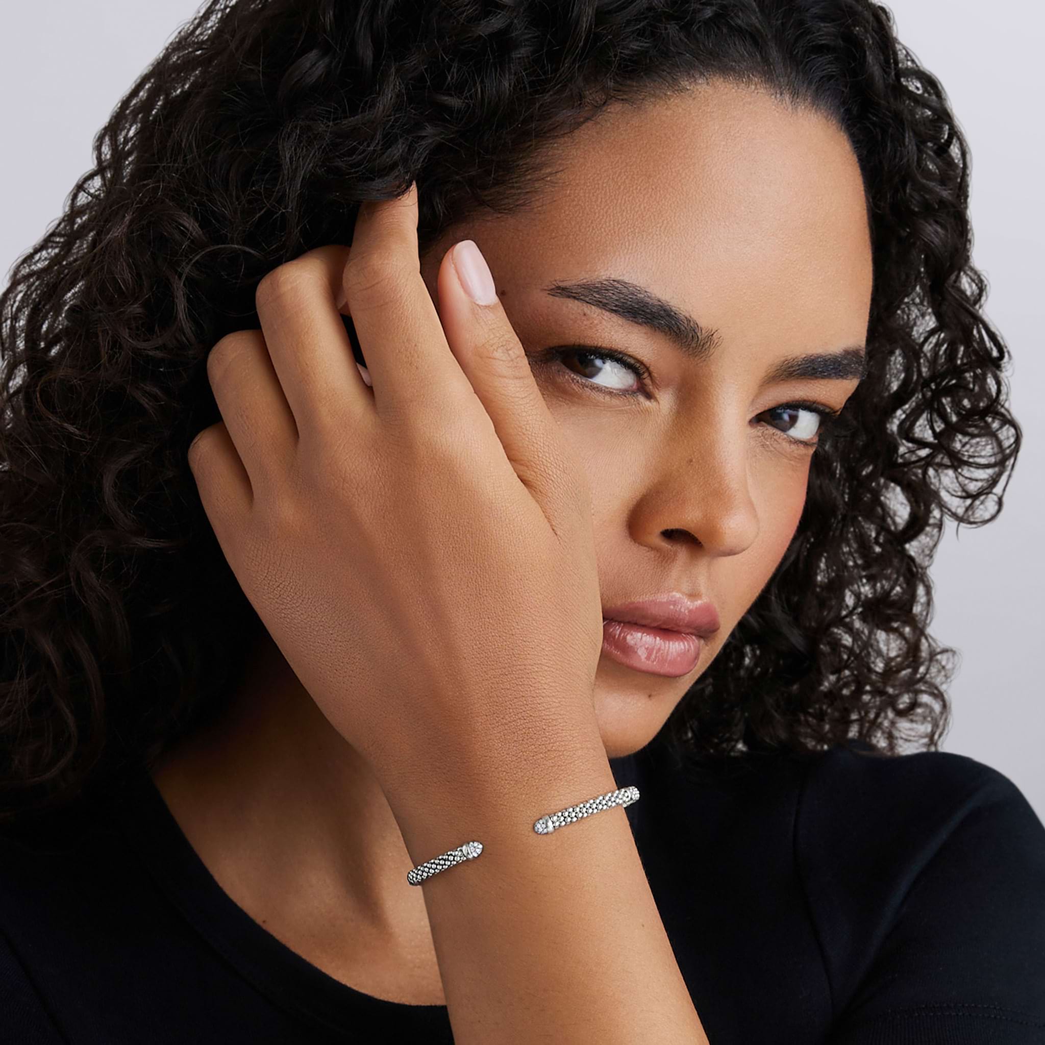 Woman's wrist adorned with LAGOS Signature Caviar Sterling Silver Diamond Mini Versa Torque Bracelet, showcasing pavé diamonds and elegant design against a minimalist backdrop.