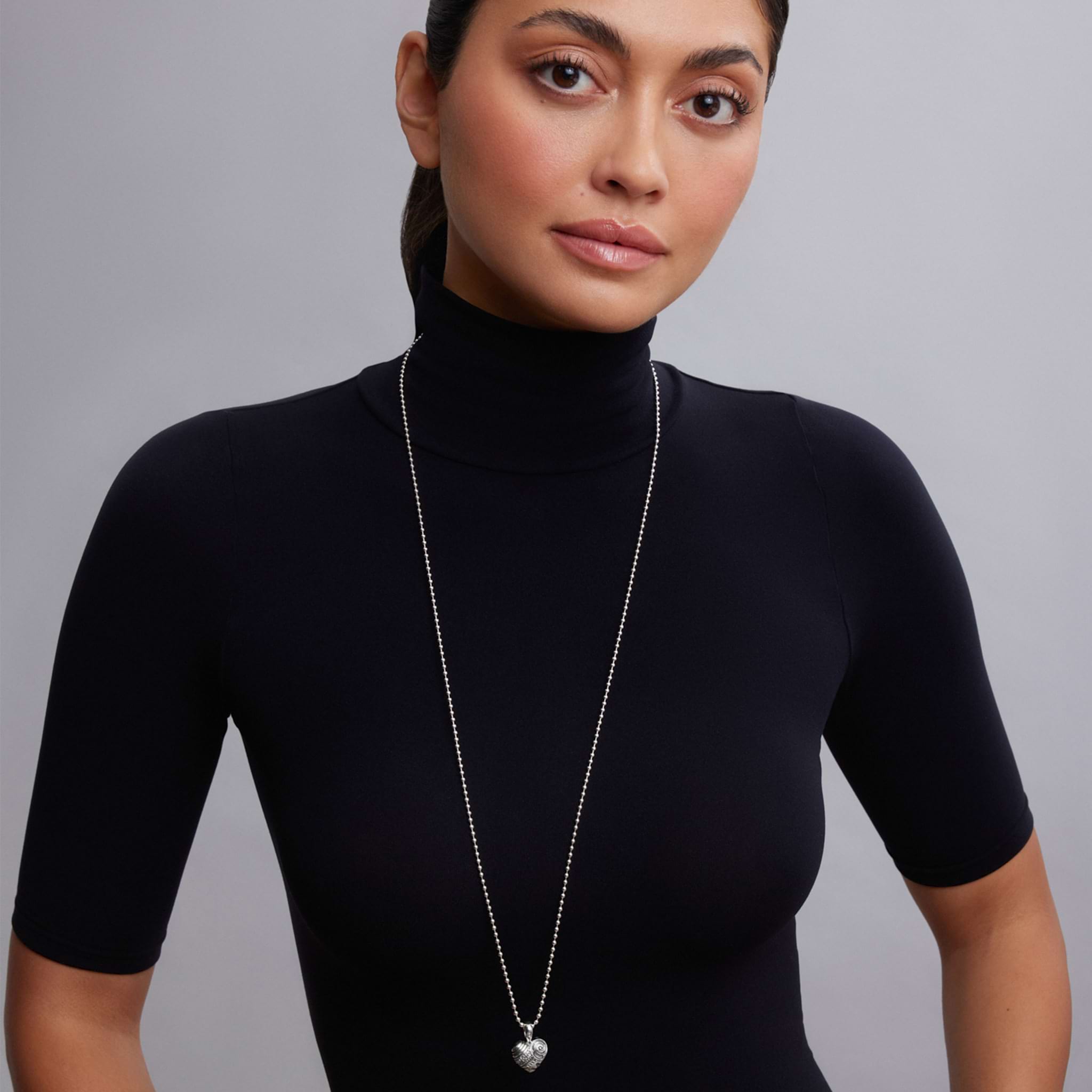 Hearts of LAGOS Silver Heart of Philadelphia Pendant Necklace shown on a model wearing a black turtleneck, featuring a detailed sterling silver heart pendant with cultural icons.