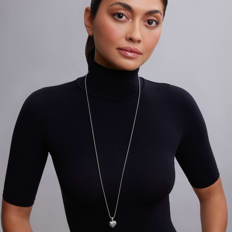 Hearts of LAGOS Silver Heart of Philadelphia Pendant Necklace shown on a model wearing a black turtleneck, featuring a detailed sterling silver heart pendant with cultural icons.