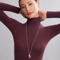 Woman wearing a maroon turtleneck and silver necklace with a gecko pendant on a gray background