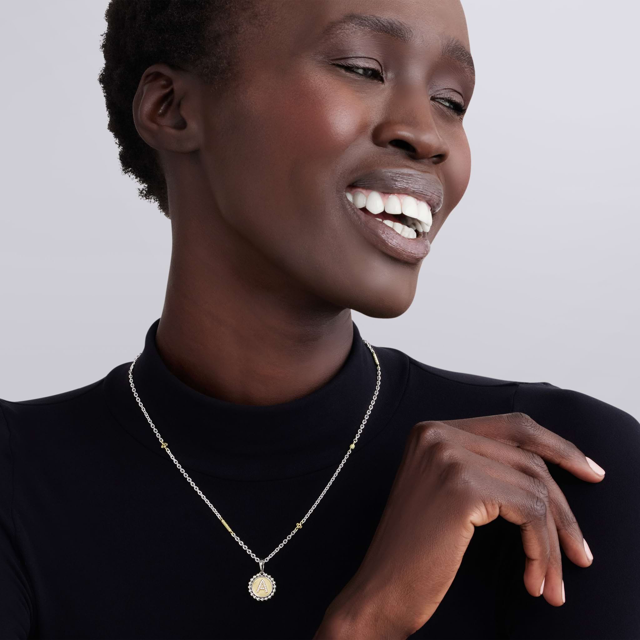 Smiling person wearing Signature Caviar T Initial Diamond Charm Necklace in sterling silver and 18K gold, featuring a diamond-accented T charm on a caviar beaded chain.