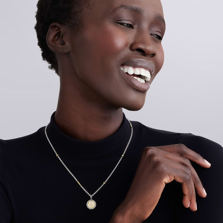Smiling person wearing Signature Caviar T Initial Diamond Charm Necklace in sterling silver and 18K gold, featuring a diamond-accented T charm on a caviar beaded chain.