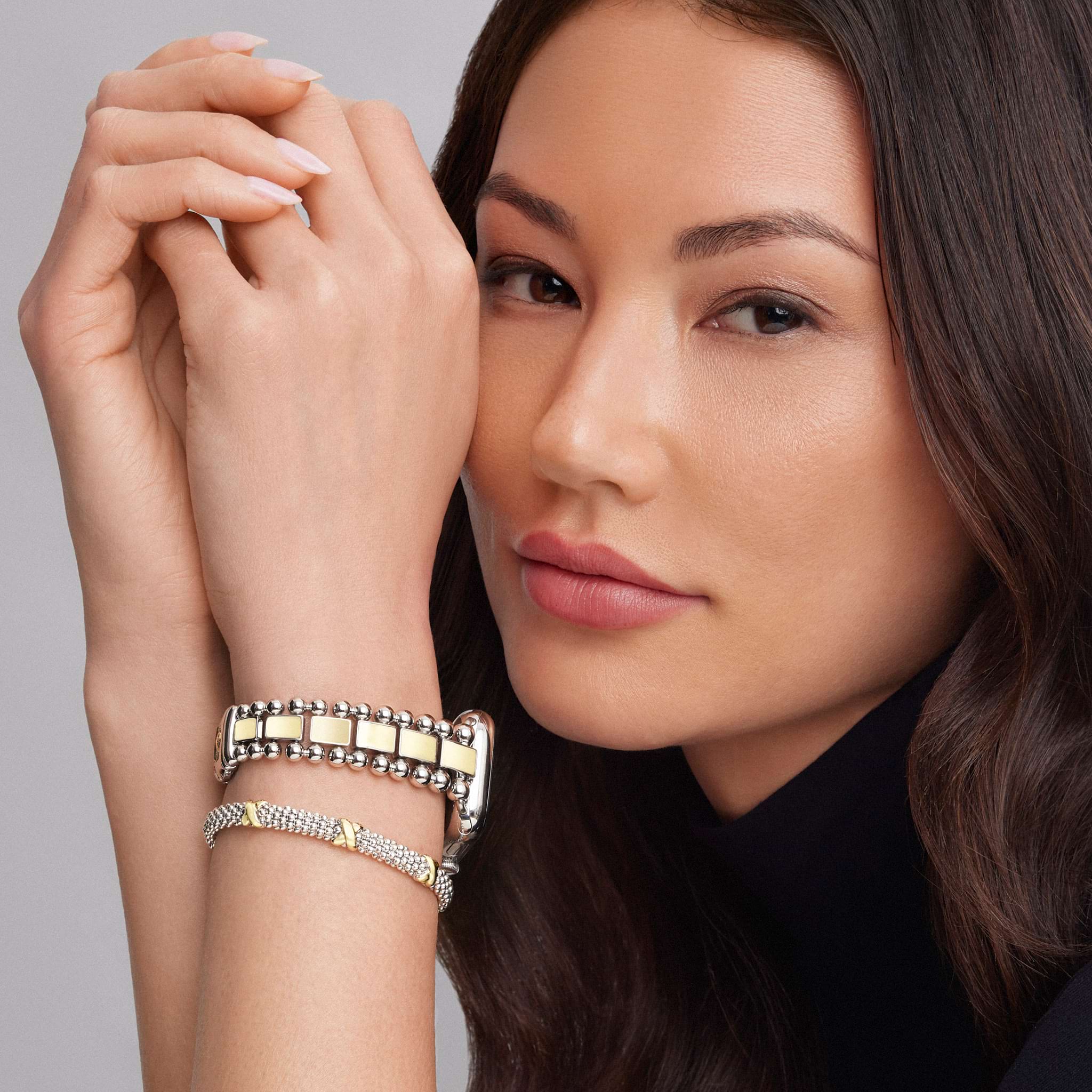 Young woman showcasing LAGOS Smart Caviar 18K Gold Smart Caviar Gift Set: polished bracelets and a watch band in sterling silver and 18K gold.