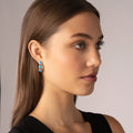 Rittenhouse Swiss Blue Topaz Hoop Earrings on a young woman, showcasing bright blue gemstones set in sterling silver and 18K gold Caviar beading.