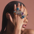 Woman showcasing Glacier Large Emerald-Cut Swiss Blue Topaz Ring in sterling silver with 18K gold Caviar beading, surrounded by colorful gemstone rings, reflecting LAGOS elegance.
