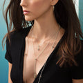 Woman wearing KSL Pyramid Lariat Necklace with geometric pendants and layered fine chains, styled with small earrings and deep-V black top.