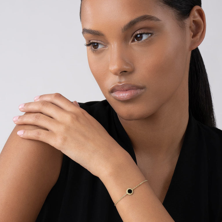 Woman wearing the Covet Single Station Round Onyx Bracelet, featuring an 18k gold chain with a black onyx inlay and Caviar beaded details, resting on her wrist.