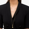 Person wearing a tailored black jacket featuring the Rare Wonders Blue Sapphire and Diamond King Pendant Necklace with an 18K gold chain and a decorative tassel pendant.