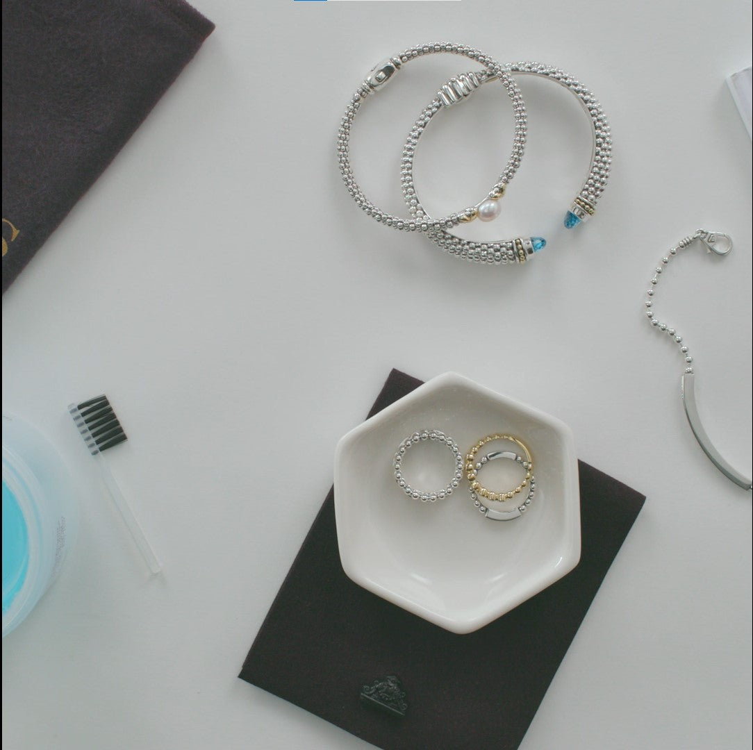 Flat-lay of jewelry with LAGOS Accessories Jewelry Cleaner, featuring bracelets, stackable rings, and a cleaning kit for pearls, diamonds, and metal.